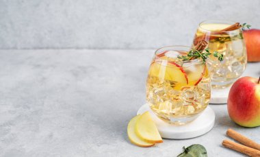İki bardak soğuk elma kokteyli ya da tarçın ve kekik ile süslenmiş buzlu elma şarabı hafif bir arka planda mermer tezgahta meyve dilimleriyle. Ferahlatıcı içecek konsepti. Boşluğu kopyala.