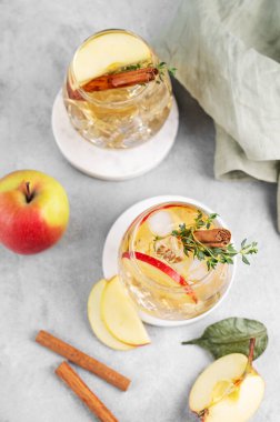 İki bardak soğuk elma kokteyli ya da tarçın ve kekik ile süslenmiş buzlu elma şarabı hafif bir arka planda mermer tezgahta meyve dilimleriyle. Ferahlatıcı içecek konsepti. Üst görünüm