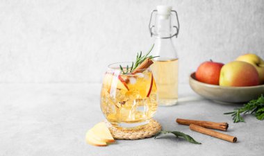 Elma kokteyli ya da buzlu elma şarabı, tarçın ve biberiyeyle süslenmiş hafif bir arka planda meyve ve şişeyle. Ferahlatıcı içecek konsepti. Ön görünüm, boşluğu kopyala