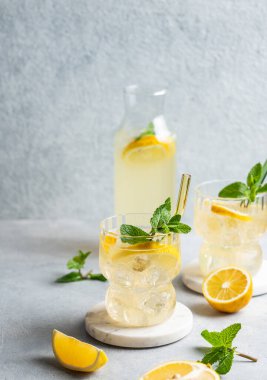 Limonlu, naneli ve buzlu iki bardak taze limonata. Arka planda hafif bir şişe, taze bitki ve meyve var. Yaz modasına uygun mojito mocktail konsepti. Ön görünüm, boşluğu kopyala