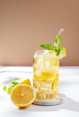 Limonlu buzlu çay ve beyaz bej arka planda bir bardakta nane şekeri. Turunçgil meyvesi ve güneş ışığı. Yaz günü ferahlatıcı içecek ya da limonata konsepti. Ön görünüm, boşluğu kopyala.