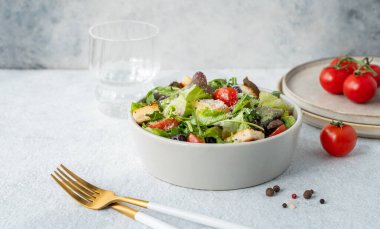 Salata, domates, kızarmış ekmek, zeytin ve parmesan peynirli vejetaryen salatası hafif bir arka planda taze sebze, bir bardak su ve çatal bıçakla birlikte. Sağlıklı beslenme konsepti. Boşluğu kopyala.