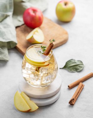 Soğuk elma kokteyli ya da buzlu bir bardakta elma şarabı, tarçın ve kekik ile süslenmiş, mermer tezgahta meyvelerle süslenmiş. İçecek konseptini tazelemek. 