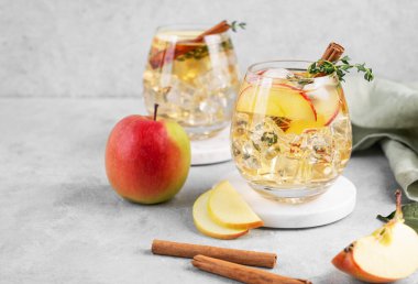 İki bardak soğuk elma kokteyli ya da tarçın ve kekik ile süslenmiş buzlu elma şarabı hafif bir arka planda mermer tezgahta meyve dilimleriyle. Ferahlatıcı içecek konsepti. Boşluğu kopyala.