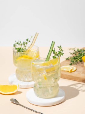 İki bardak mocktail mojito, limon, limon, kekik ve buz. Sarı arka planda meyveli turunçgil limonatası. Yaz modasına uygun soğuk içecek konsepti. Ön görünüm, boşluğu kopyala.