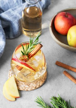 Elma kokteyli ya da buzlu elma şarabı, tarçın ve biberiyeyle süslenmiş hafif bir arka planda meyve, peçete ve şişeyle birlikte. Ferahlatıcı içecek konsepti. Üst görünüm