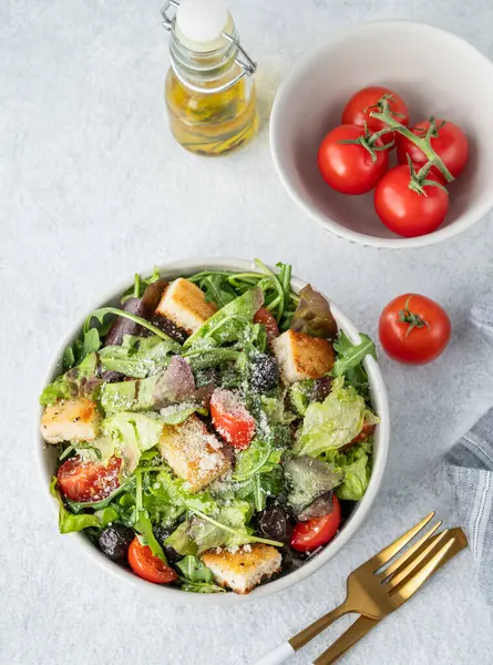 Salata, marul, domates, kızarmış ekmek, zeytin ve parmesan peyniri taze sebze, yağ ve çatal bıçakla hafif bir arka planda. Sağlıklı beslenme konsepti. Üst görünüm, alanı kopyala.