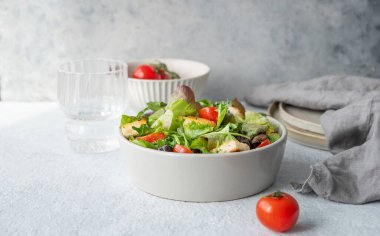 Hafif bir zemin üzerinde taze sebzeler ve bir bardak suyla bir kasede marul, domates, kızarmış ekmek ve zeytinli vejetaryen salatası. Sağlıklı beslenme konsepti. Ön görünüm, boşluğu kopyala.