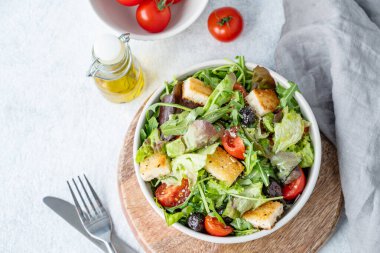 Marul, domates, kızarmış ekmek ve zeytinli vejetaryen salatası taze sebze, yağ ve çatal bıçakla birlikte tahta bir tabakta. Sağlıklı beslenme konsepti. Üst görünüm, alanı kopyala.