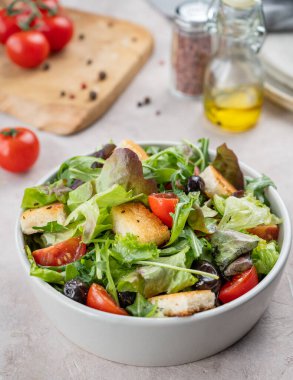 Baharat ve yağla kaplanmış hafif arka planda bir kasede marul, domates, kızarmış ekmek ve zeytinli sebze salatası. Sağlıklı beslenme konsepti. Üst görünüm.