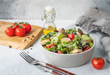 Marul, domates, kızarmış ekmek, zeytin ve parmesan peynirli vejetaryen salatası hafif bir arka planda taze sebze, yağ ve çatal bıçakla birlikte. Sağlıklı beslenme konsepti. 