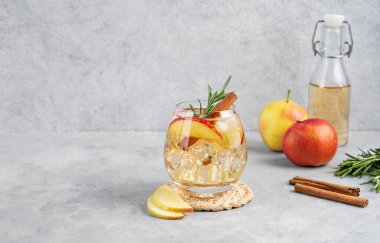 Elma kokteyli ya da buzlu elma suyu, tarçın ve biberiye ile süslenmiş hafif bir arka planda meyve ve şişe dilimleriyle birlikte. Ferahlatıcı içecek konsepti. Ön görünüm, boşluğu kopyala