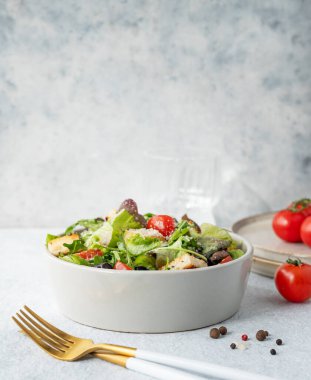 Salatalı, domatesli, kızarmış ekmekli, zeytinli ve parmesan peynirli vejetaryen salatası hafif bir arka planda taze sebze, baharat ve çatal bıçakla. Sağlıklı beslenme konsepti. Ön görünüm, boşluğu kopyala