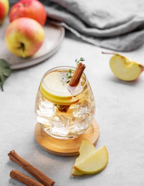 Soğuk elma kokteyli ya da buzlu bir bardakta elma şarabı, tarçın ve kekik ile süslenmiş hafif bir arka planda meyvelerle. İçecek konseptini tazelemek. 