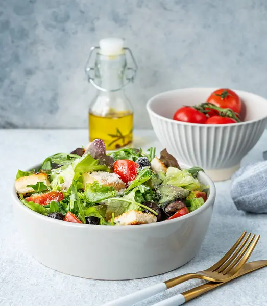 Salata, marul, domates, kızarmış ekmek, zeytin ve parmesan peyniri taze sebze, yağ ve çatal bıçakla hafif bir arka planda. Sağlıklı beslenme konsepti. Ön görünüm, boşluğu kopyala.