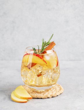 Elma kokteyli ya da buzlu elma şarabı, tarçın ve biberiyeyle süslenmiş hafif arka planda bir bardakta meyve dilimi ile. Ferahlatıcı içecek konsepti. Ön görünüm, boşluğu kopyala