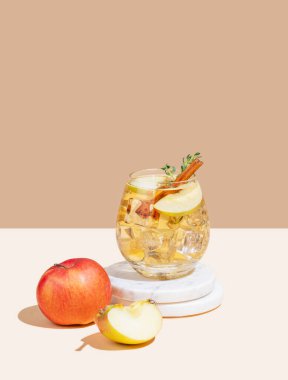 Elma kokteyli ya da elma şarabı buzlu, tarçınlı ve kekikli beyaz bej arka plandaki mermer tezgahta. Reklamcılık ya da bar menüsü afişi için canlandırıcı içecek konsepti. Ön görünüm, boşluğu kopyala