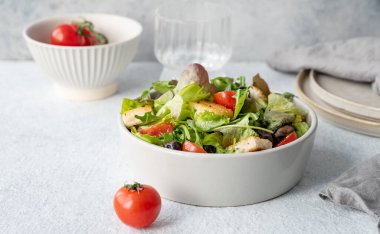 Hafif arka planda bir kasede salata, domates, kızarmış ekmek ve zeytinli taze sebze ve bir bardak suyla birlikte. Sağlıklı beslenme konsepti. Ön görünüm, boşluğu kopyala.