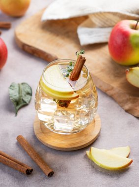 Soğuk elma kokteyli ya da buzlu bir bardakta elma şarabı, tarçın ve kekik ile süslenmiş hafif bir arka planda meyve dilimi. İçecek konseptini tazelemek. 
