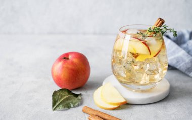 Elma kokteyli ya da buzlu elma şarabı, tarçın ve kekik ile süslenmiş mermer tezgahta hafif bir arka planda meyve dilimi ile. Ferahlatıcı içecek konsepti. Ön görünüm, boşluğu kopyala