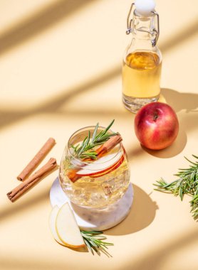 Elma kokteyli ya da buzlu bir bardakta elma şarabı, tarçın ve biberiye mermer bir tezgahta gölgeli sarı bir arka planda. Reklam veya bar menüsü afişi için içki konsepti. Üst görünüm, alanı kopyala