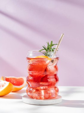 Beyaz pembe arka planda gölgeli bir bardakta greyfurt, biberiye ve buzla mocktail tazeleyici. Yaz turunçgil içeceği ya da kafe reklamları için limonata konsepti. Ön görünüm