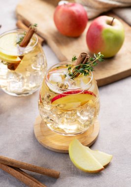 İki bardak soğuk elma kokteyli ya da tarçın ve kekik ile süslenmiş buzlu elma şarabı hafif bir arka planda meyve dilimleriyle. İçecek konseptini tazelemek. 