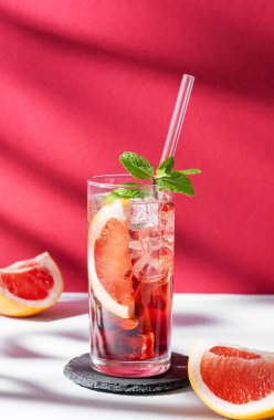 Üzüm suyu, nane ve buzlu kokteyl beyaz kırmızı arka planda gölgesi ve güneş ışığı olan bir bardakta. Yaz turunçgilleri ya da limonata konsepti. Ön görünüm ve boşluk kopyala.