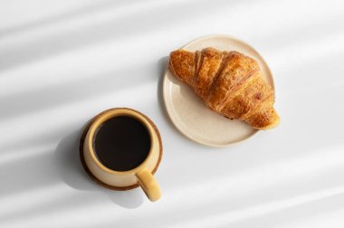 Sarı fincanlı kahve espresso ve beyaz arka planda sabah gölgeli taze kruvasan. Yaratıcı tasarım ve sağlıklı yemek ve Fransız kahvaltısı konsepti. Üst görünüm, alanı kopyala.
