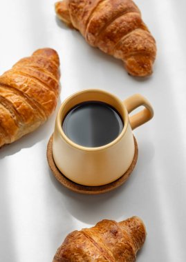 Sarı fincanlı kahve espresso ve beyaz arka planda sabah gölgeli taze kruvasan. Yaratıcı tasarım ve sağlıklı yemek ve Fransız kahvaltısı konsepti. Üst görünüm