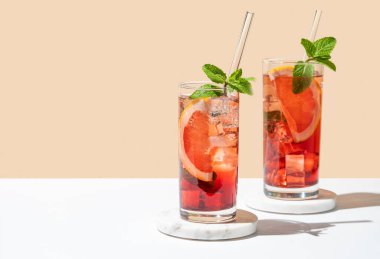 İki bardak kokteyl, greyfurtlu, naneli ve buzlu mermer üzerine beyaz sarı arka planda, gölgeli. Yaz turunçgilleri ya da limonata konsepti. Ön görünüm ve boşluk kopyala.