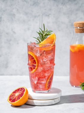 Buzlu ve biberiyeli kan portakalı kokteyli gri arka planda, şişeli mermer bir tezgahta. Kafe menüsü reklam afişi için yaz turunçusu içeceği konsepti. Ön görünüm, boşluğu kopyala.