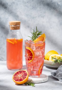 Mermer bir tezgahta buzlu ve biberiyeli kan portakalı kokteyli. Gölgeler ve şişelerle dolu gri bir arka plan. Kafe menüsü reklam afişi için yaz turunçusu içeceği konsepti. Ön görünüm
