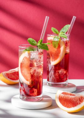 İki bardak kokteyl, greyfurtlu, naneli ve buzlu mermer üzerine kırmızı beyaz arka planda, gölgeli. Yaz turunçgilleri ya da limonata konsepti. Ön görünüm ve boşluk kopyala.