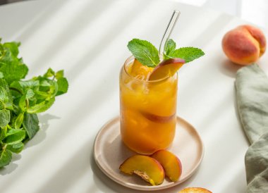 Şeftali ya da buzlu çay, beyaz bir masada bir bardakta nane şekeri taze meyve, otlar, peçete ve güneş ışığı. Bar ya da kafe menüsü için yaz kokteyli konseptini tazeliyorum. Üst görünüm, alanı kopyala.