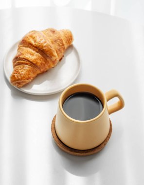 Sarı fincanlı kahve espresso ve beyaz arka planda sabah gölgeli taze kruvasan. Yaratıcı tasarım ve sağlıklı yemek ve Fransız kahvaltısı konsepti. Üst görünüm, alanı kopyala.