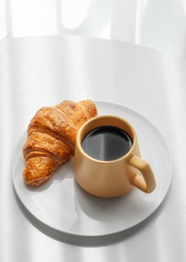 Kahve espresso sarı fincanda ve taze kruvasan beyaz bir tabakta sabah gölgeli pencerenin yanında. Yaratıcı tasarım ve sağlıklı yemek ve Fransız kahvaltısı konsepti. Üst görünüm, alanı kopyala.