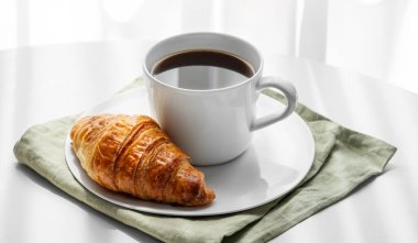 Bir fincan espresso kahve ve peçete üzerine taze kruvasan. Pencerenin yanındaki beyaz masada, sabah gölgeli. Menü için reklam pankartı ya da sağlıklı yemek ve Fransız kahvaltı konsepti. Boşluğu kopyala.