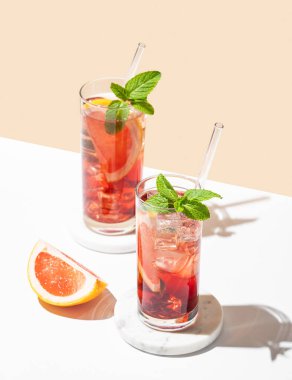 İki bardak kokteyl, greyfurtlu, naneli ve buzlu mermer üzerine beyaz sarı arka plan, gölge ve narenciye dilimli. Yaz içeceği ya da limonata konsepti. Üst görünüm ve kopyalama alanı.