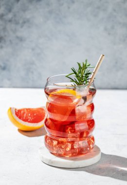 Greyfurtlu limonata, biberiye ve gölgeli arka planda hafif bir bardakta buz. Yaz turunçgil içeceği ya da kafe menüsü reklam afişi için kokteyl konsepti. Ön görünüm, boşluğu kopyala.