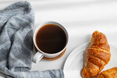 Kahve fincanı ve beyaz arka planda sabah gölgesi ve peçeteli taze kruvasanlar. Yaratıcı tasarım ve sağlıklı yemek ve Fransız kahvaltısı konsepti. Üst görünüm ve kopyalama alanı.