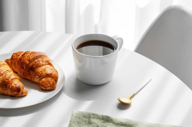 Bir fincan espresso kahve ve taze kruvasan. Sabah gölgesi ve peçetesi olan beyaz bir masada. Menü ya da sağlıklı yemek ve Fransız kahvaltı konsepti için reklam pankartı. 