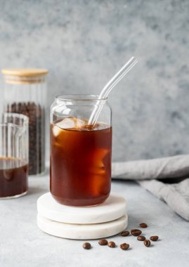 Soğuk kahve bardağında, mermer tezgahta buzlu kahve fonu ve kahve çekirdekleri. Moda yazlık ferahlatıcı içecek. Ön görünüm, boşluğu kopyala.