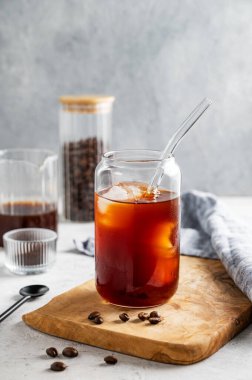 Kahve çekirdekleri ve peçeteyle arka planda, tahta bir tahtada buzlu soğuk demlenmiş kahve bardağı. Moda yazlık ferahlatıcı içecek. Ön görünüm, boşluğu kopyala.