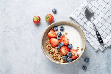 Doğal yoğurt, granola, yabanmersini ve çilek arkaplanda taze böğürtlen ve kaşıkla birlikte. Sağlıklı, besleyici ve besleyici kahvaltı kavramı. Üst görünüm, alanı kopyala.