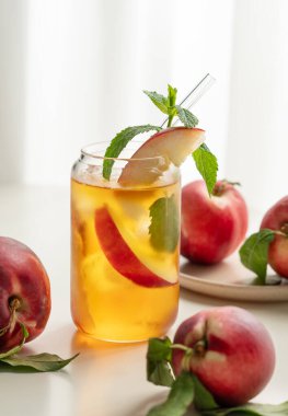 Şeftalili buzlu çay, pencerenin yanındaki beyaz masada bardakta nane şekeri taze meyve ve güneş ışığı. Bar ya da kafe menüsü için yaz içeceği konsepti. Ön görünüm, boşluğu kopyala.