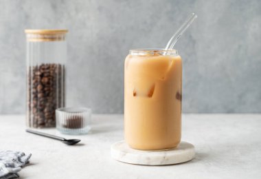 Kahve çekirdekleri ve kaşıkla hafif arkaplanlı mermer bir tahtada sütlü buzlu latte kahve. Moda yazlık ferahlatıcı içecek konsepti. Ön görünüm, boşluğu kopyala.