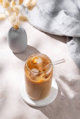 Açık arkaplanda sütlü buzlu latte kahve, kuru buket çiçekleri ve sabah gölgeleri. Moda yazlık ferahlatıcı içecek konsepti. Üst görünüm, alanı kopyala.