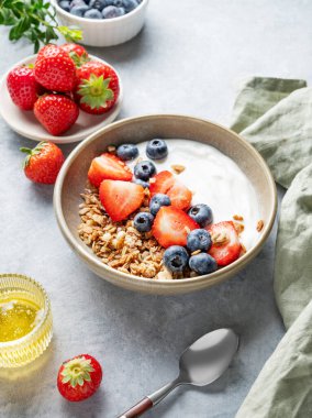 Doğal yoğurt, granola, yabanmersini ve çilek arkaplanda taze böğürtlen, bal ve kaşık. Sağlıklı, besleyici ve besleyici kahvaltı kavramı.. 