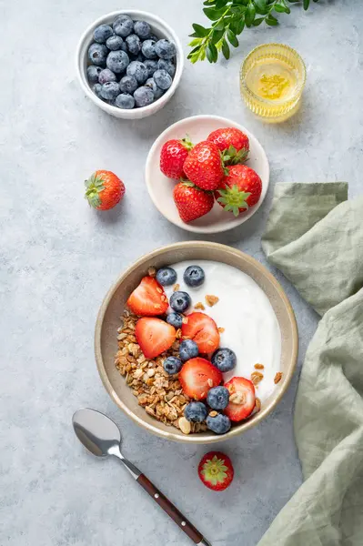 Mısır gevreği, yabanmersini ve çilekli yoğurt hafif bir arka planda taze böğürtlen ve bal ile birlikte bir kasede. Sağlıklı, besleyici ve besleyici kahvaltı kavramı. Üst görünüm, alanı kopyala.